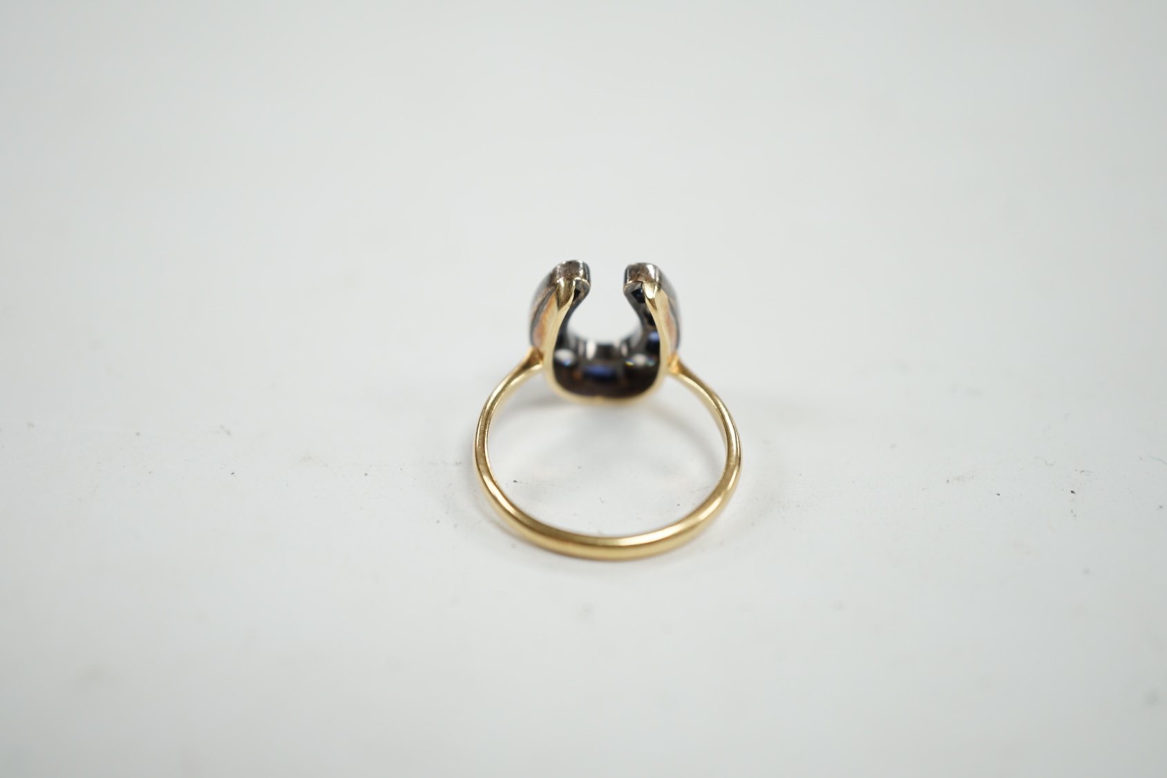 An early 20th century yellow metal (stamped 15), sapphire and diamond cluster set horseshoe shaped ring, size M, gross weight 2.8 grams. Condition - poor to fair